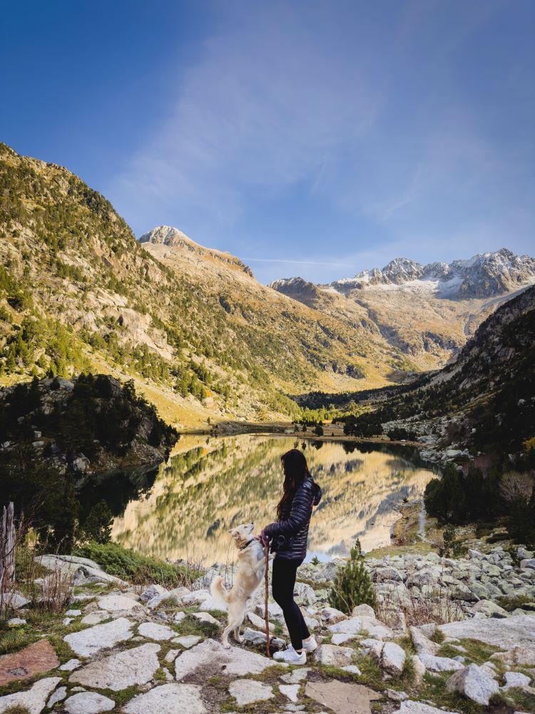 lago alta montaña y chica cogiendo a perro pequeño de las patas de delante y mirándose mutuamente en lleida